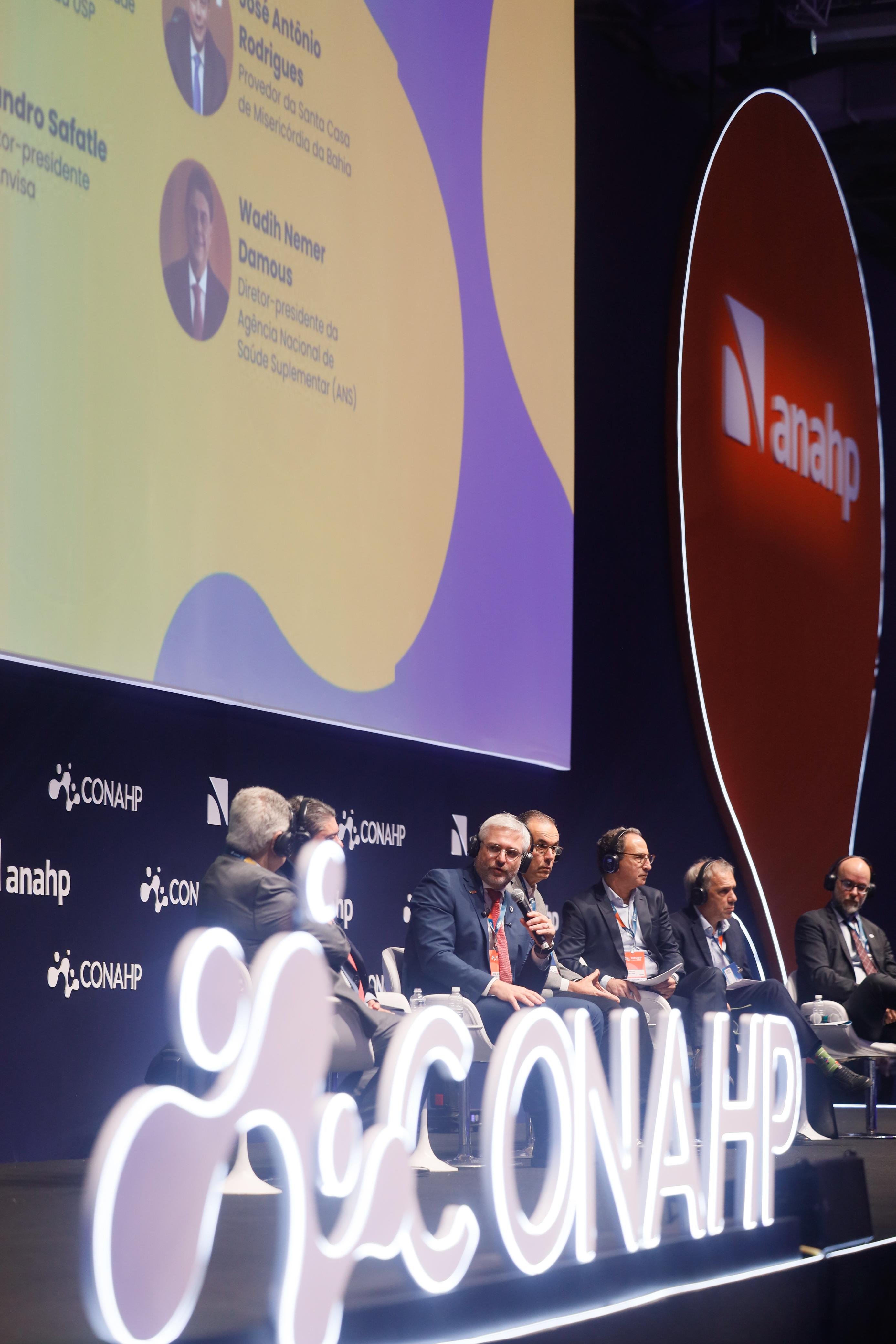 Debate no palco principal do Conahp 2025 com painelistas e o letreiro Conahp iluminado